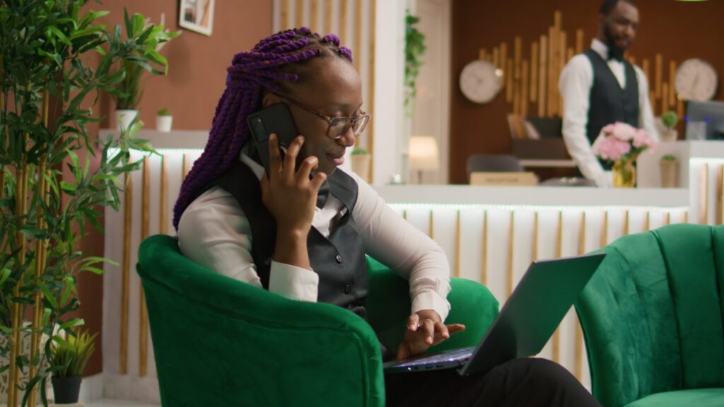 Empleada de hotel atiende una reserva por teléfono con una laptop en el lobby